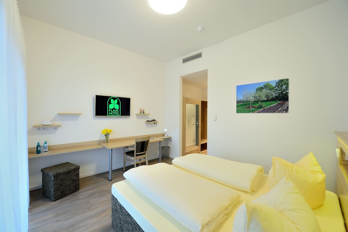 A hotel room with a bed, desk, chair, and a TV displaying the hotel name.