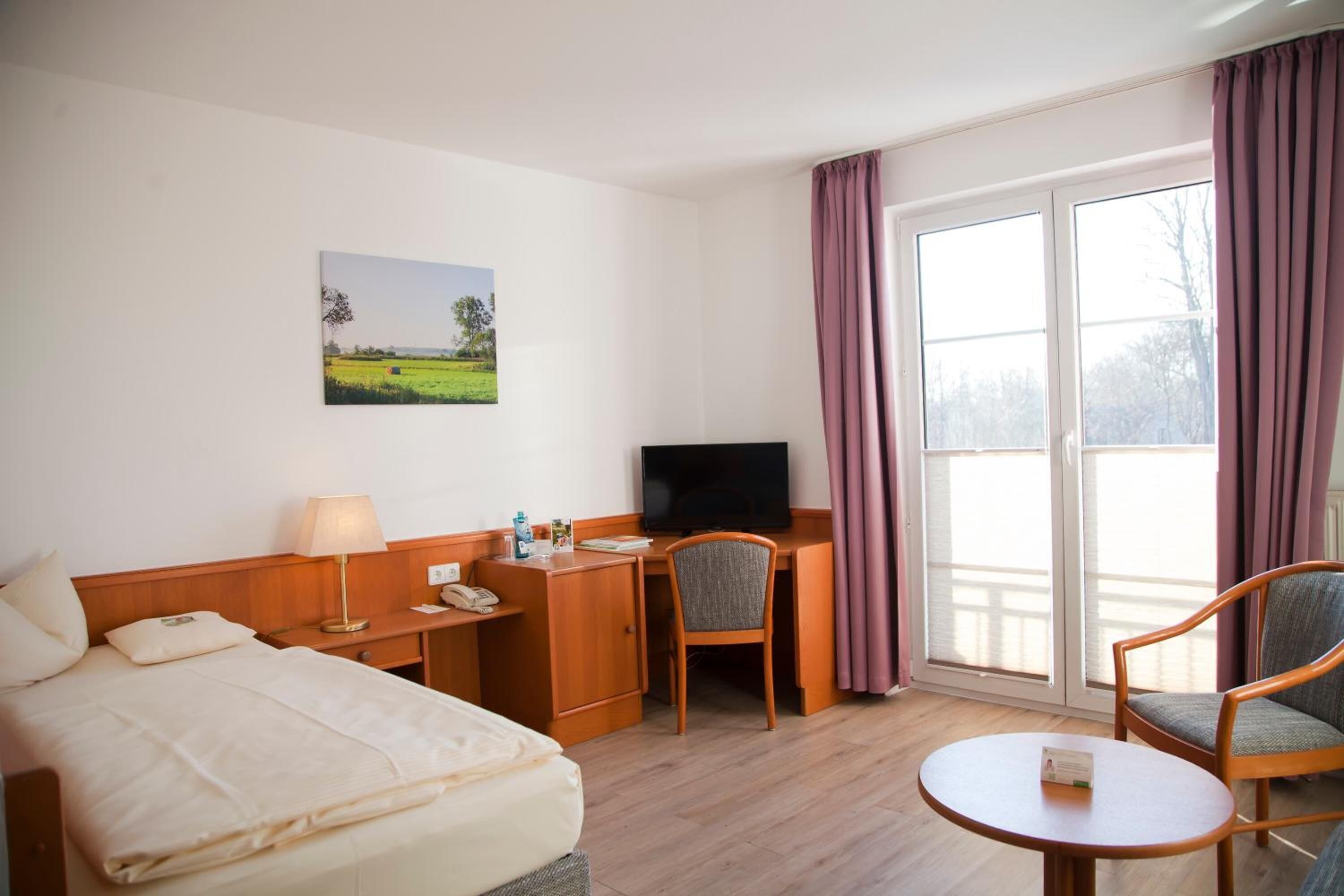 Habitación de hotel con cama, escritorio con televisor, silla, mesita y ventana con cortinas.