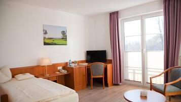 Habitación de hotel con cama, escritorio con televisor, silla, mesita y ventana con cortinas.