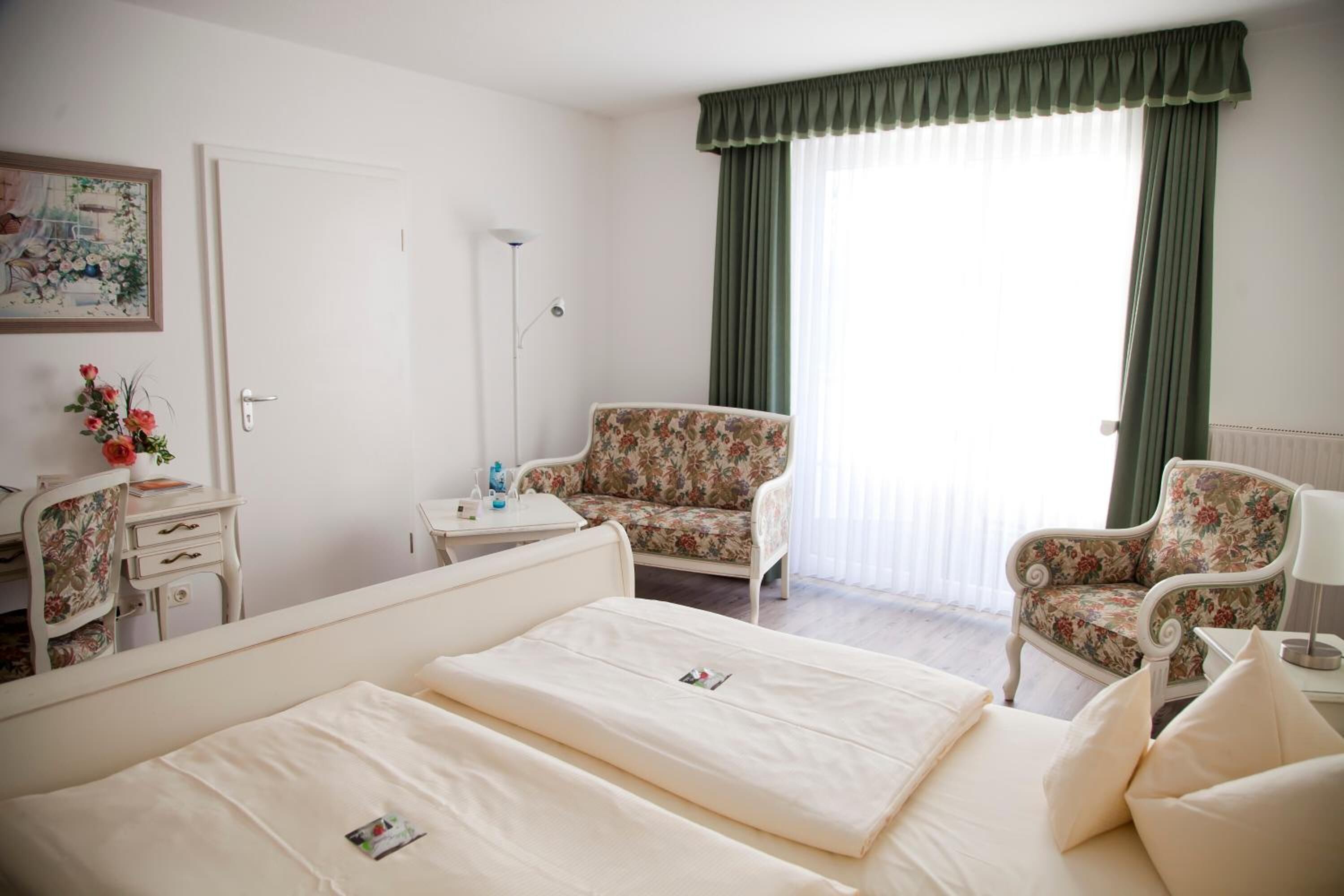A hotel room with two beds, a desk, a chair, and a large window with curtains.