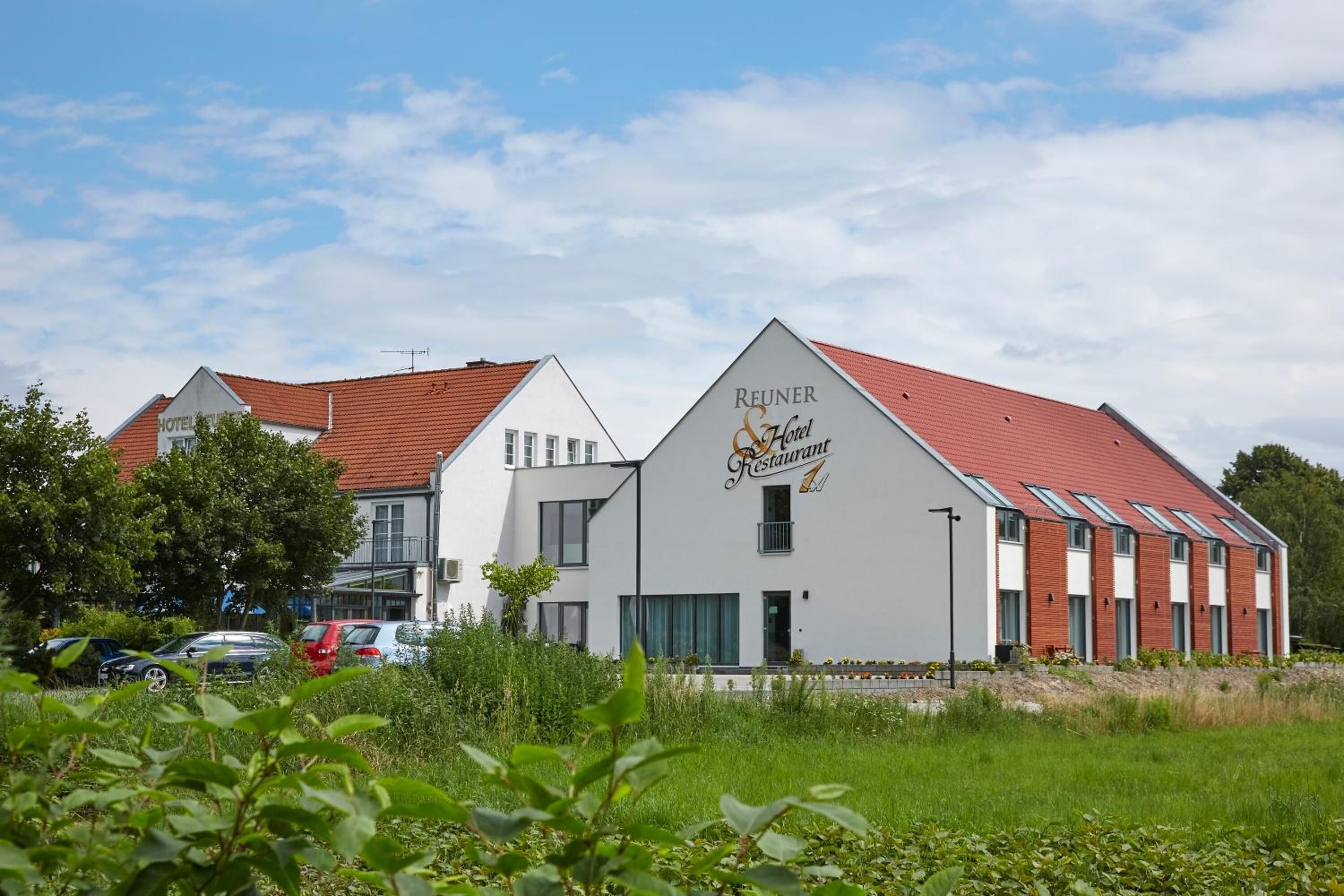 Un hôtel moderne avec un toit rouge et une façade blanche, appelé « Reuner & Hotel Restaurant ».