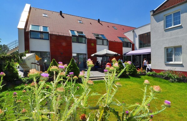 A modern building with a red-tiled roof, multiple windows, and a well-maintained garden with thistle plants. - Flair Hotel Reuner (Zossen)
