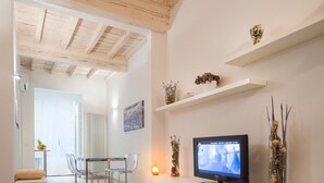 A modern living room with a wooden ceiling, a TV on a white cabinet, and a dining area with a table and chairs. - Novella Apartments (Florence)