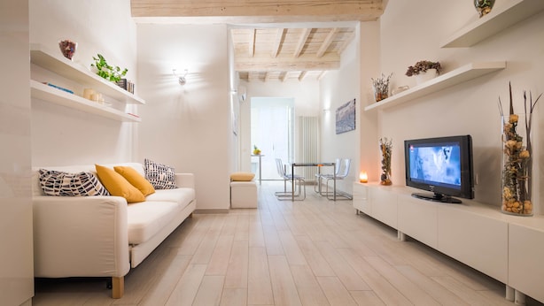 A modern living room with a white sofa, a flat-screen TV, and built-in shelves. - Novella Apartments (Florence)