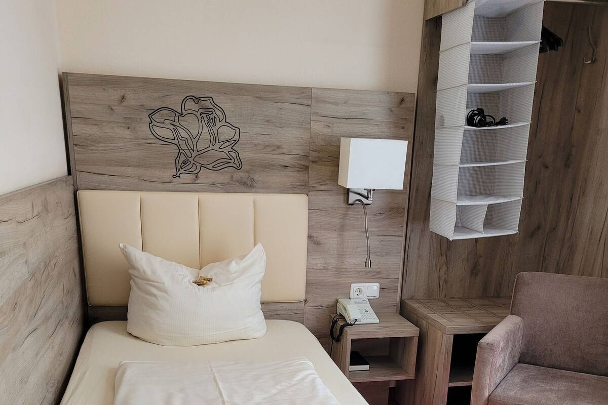 A single bed with a quilted blanket, a bedside table with a phone, and a chair.