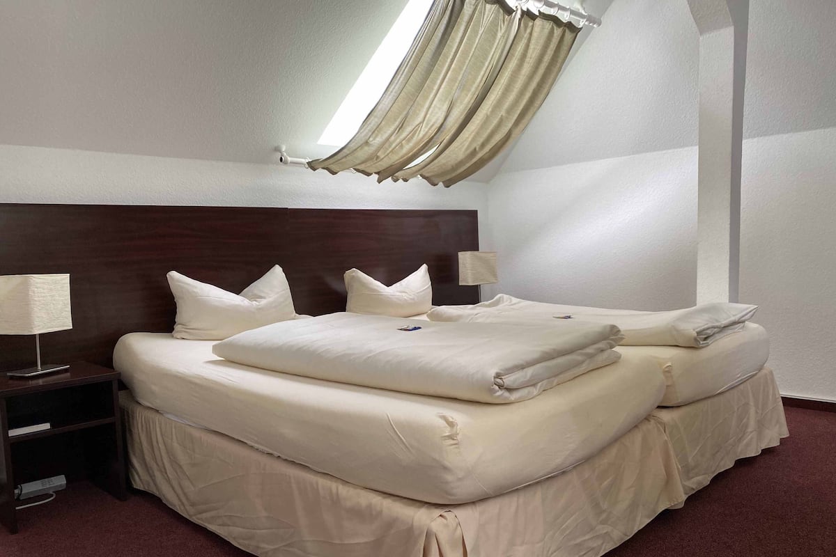 A hotel room with a large bed, two bedside tables, a nightstand, and a window with curtains.