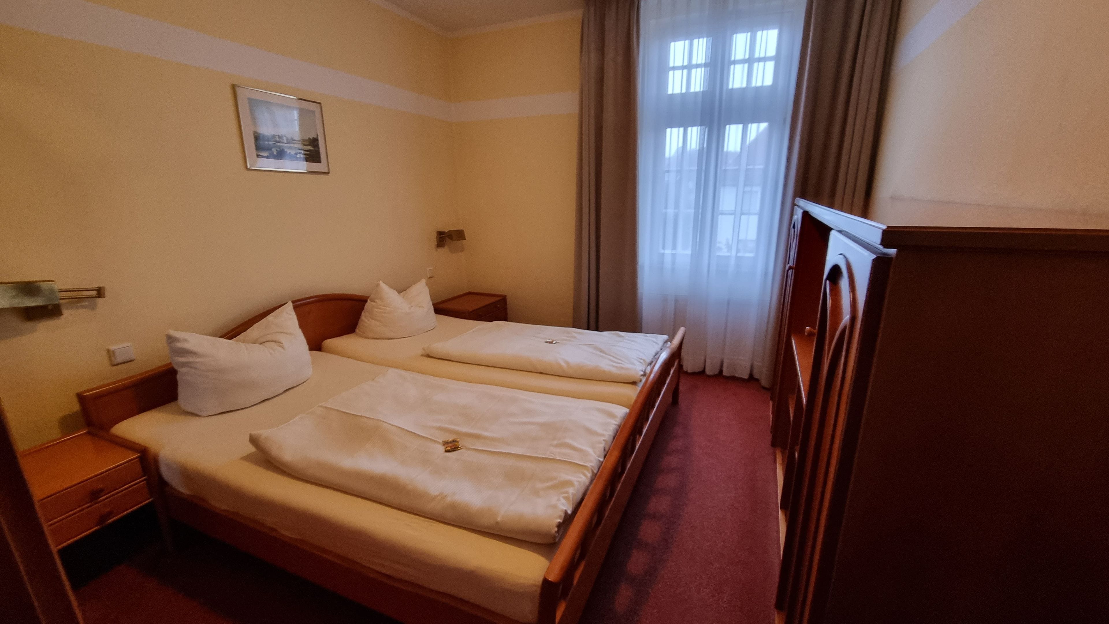A hotel room with a double bed, a bedside table, a nightstand, a chair, and a window with curtains.