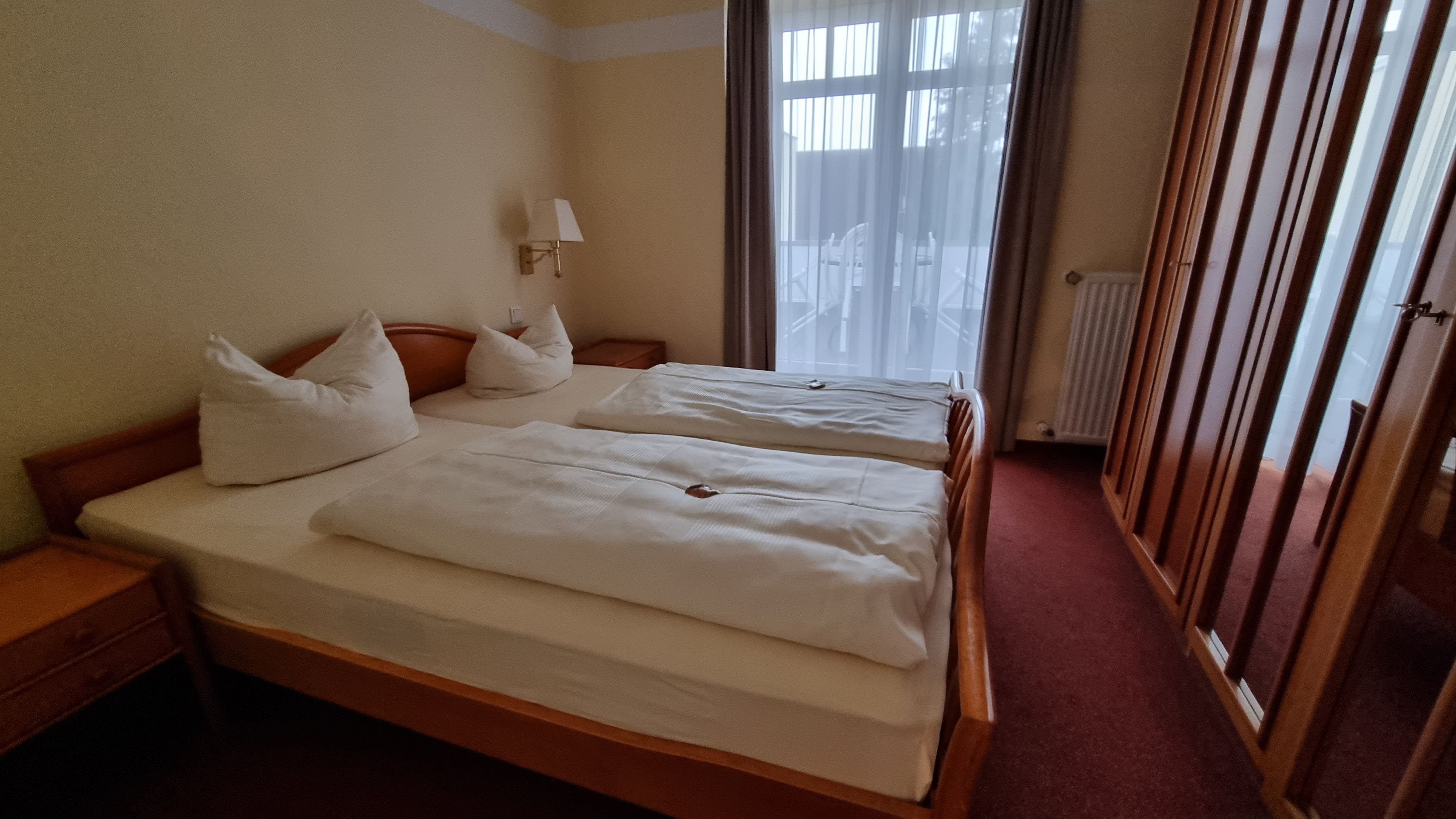 A hotel room with two beds, a nightstand, a lamp, and a window with curtains.