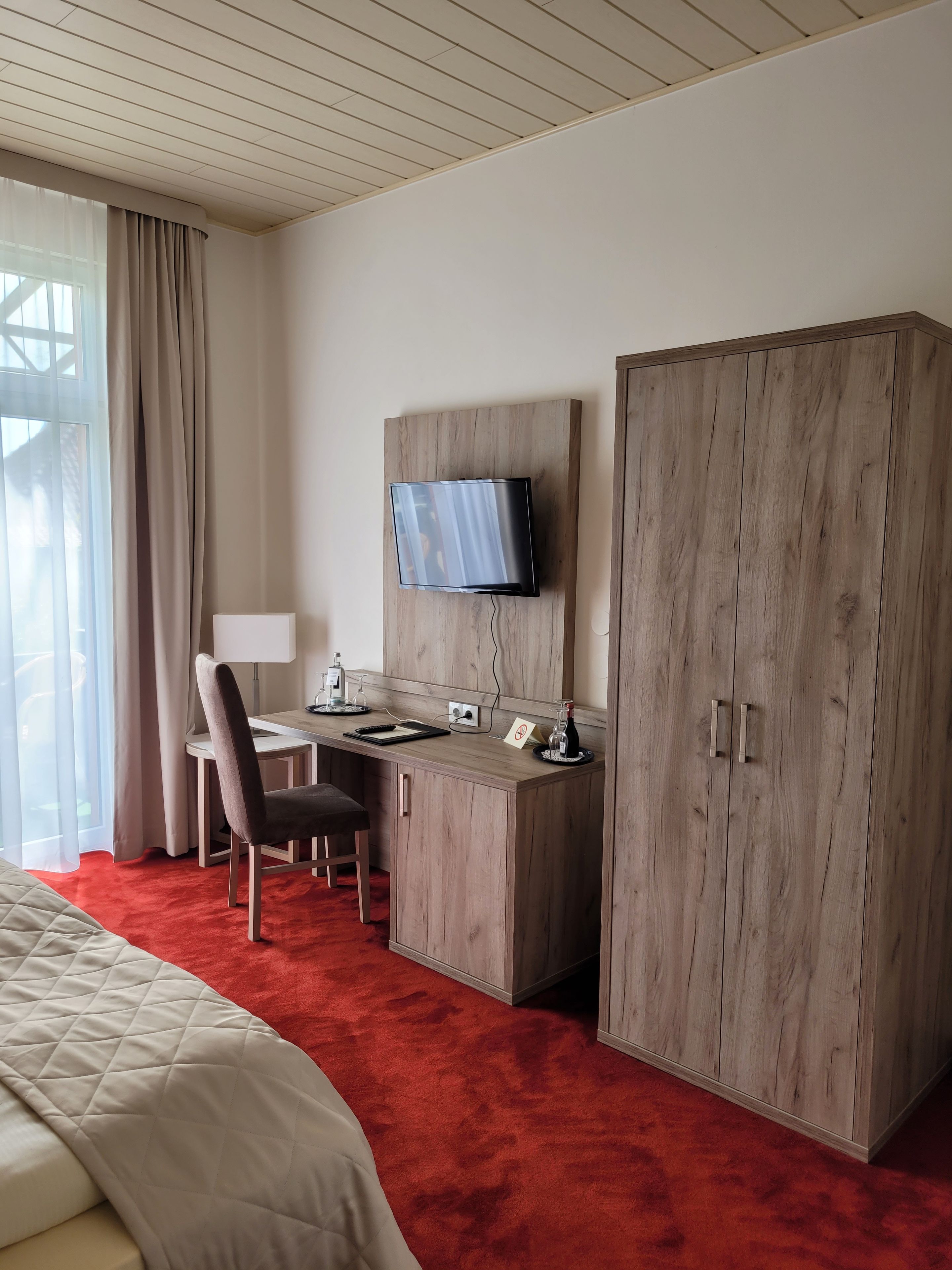 Ein Hotelzimmer mit einem Bett, einem Schreibtisch, einem Stuhl, einem an der Wand montierten Fernseher und einem Kleiderschrank.