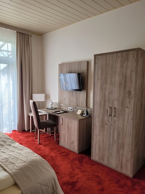 A hotel room with a bed, a desk, a chair, a television mounted on the wall, and a wardrobe. - Hotel Rosengarten (Bad Salzuflen)