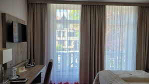 A hotel room with a bed, a desk with a TV, a chair, and a window with curtains. - Hotel Rosengarten (Bad Salzuflen)