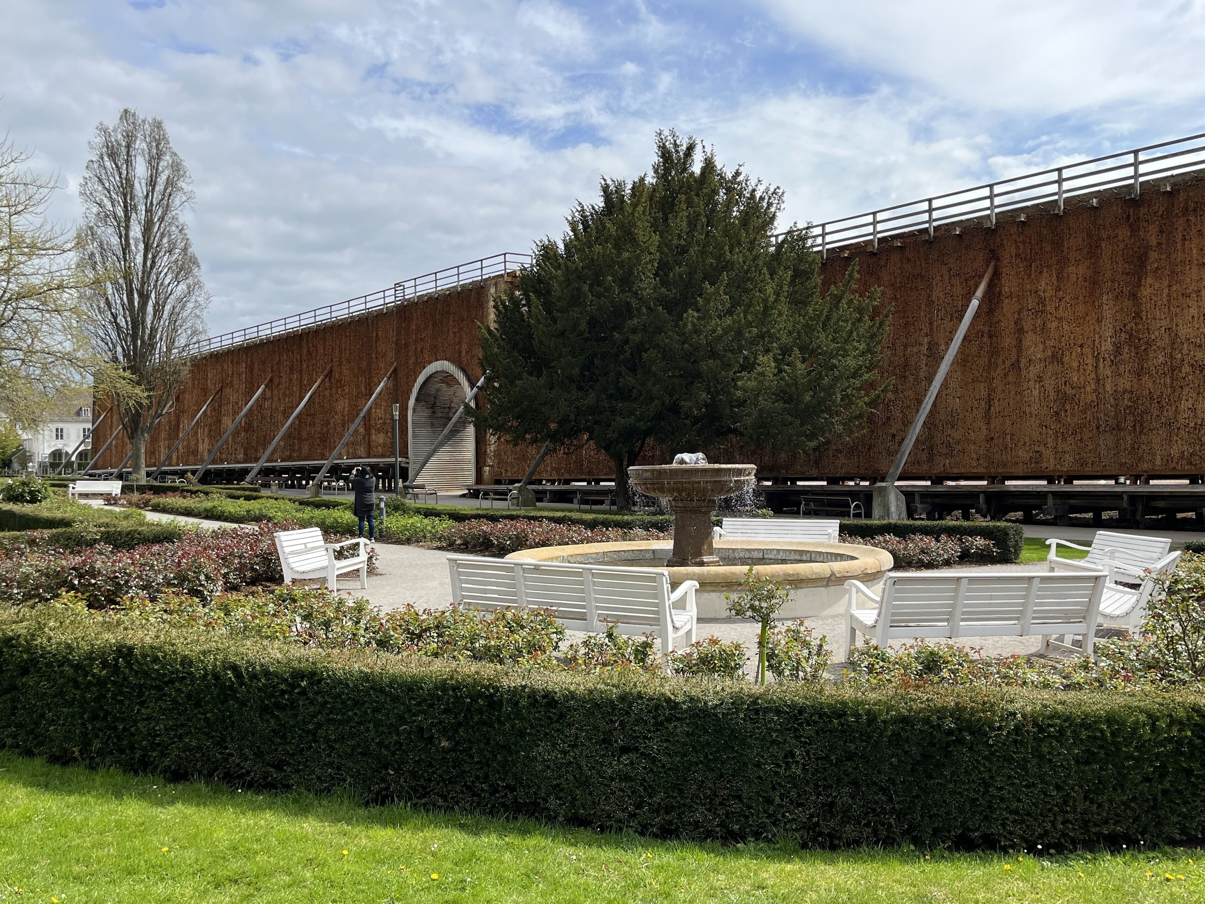 A courtyard with a fountain, benches, and a building with a wooden facade.
