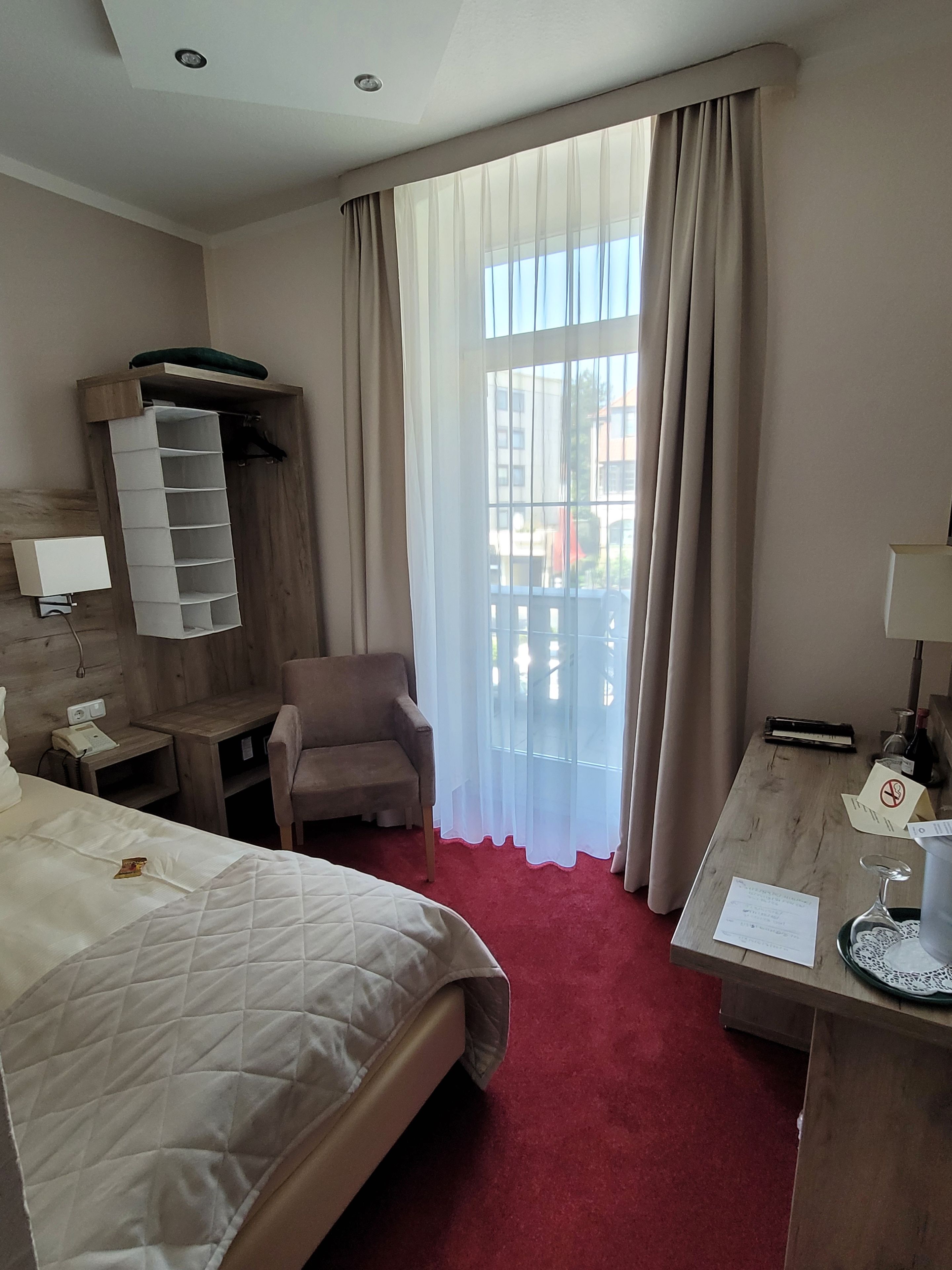 A hotel room with a bed, a desk, a chair, a wardrobe, and a window with curtains.