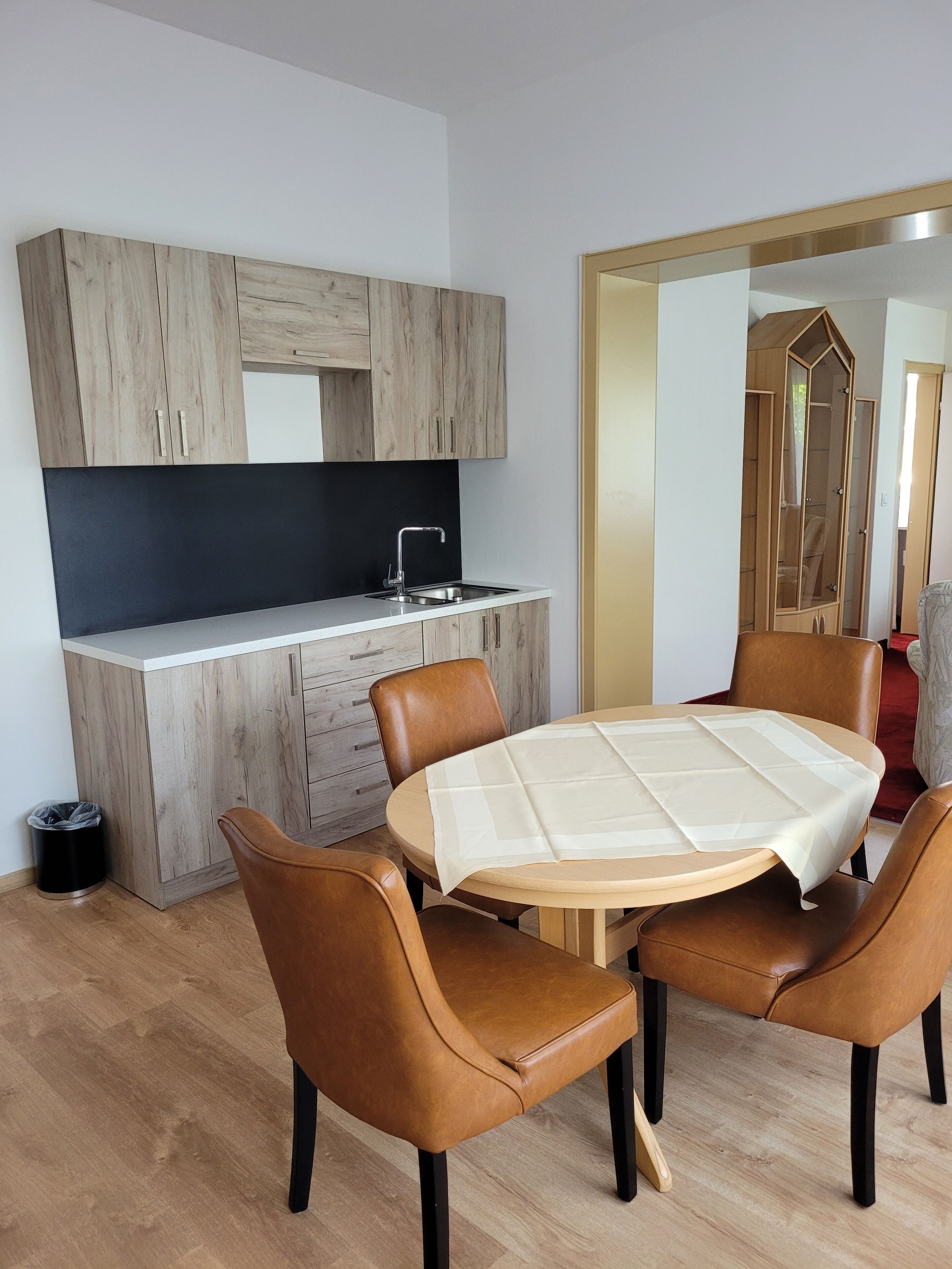 A modern kitchen with wooden cabinets, a black countertop, and a sink. There is a dining area with a round table and four brown leather chairs.