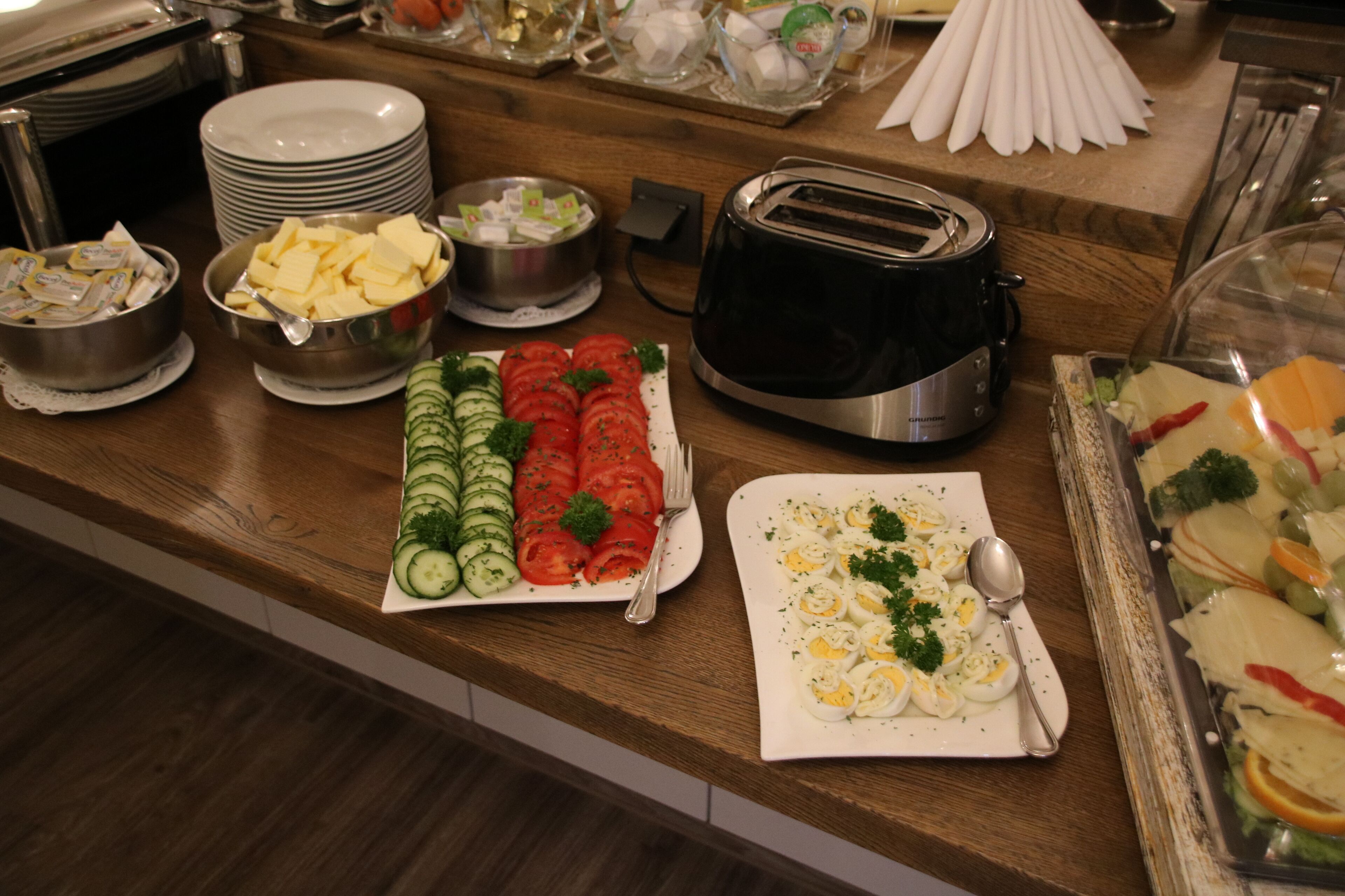 A buffet counter with various food items including sliced cucumbers, tomatoes, and a plate of eggs.