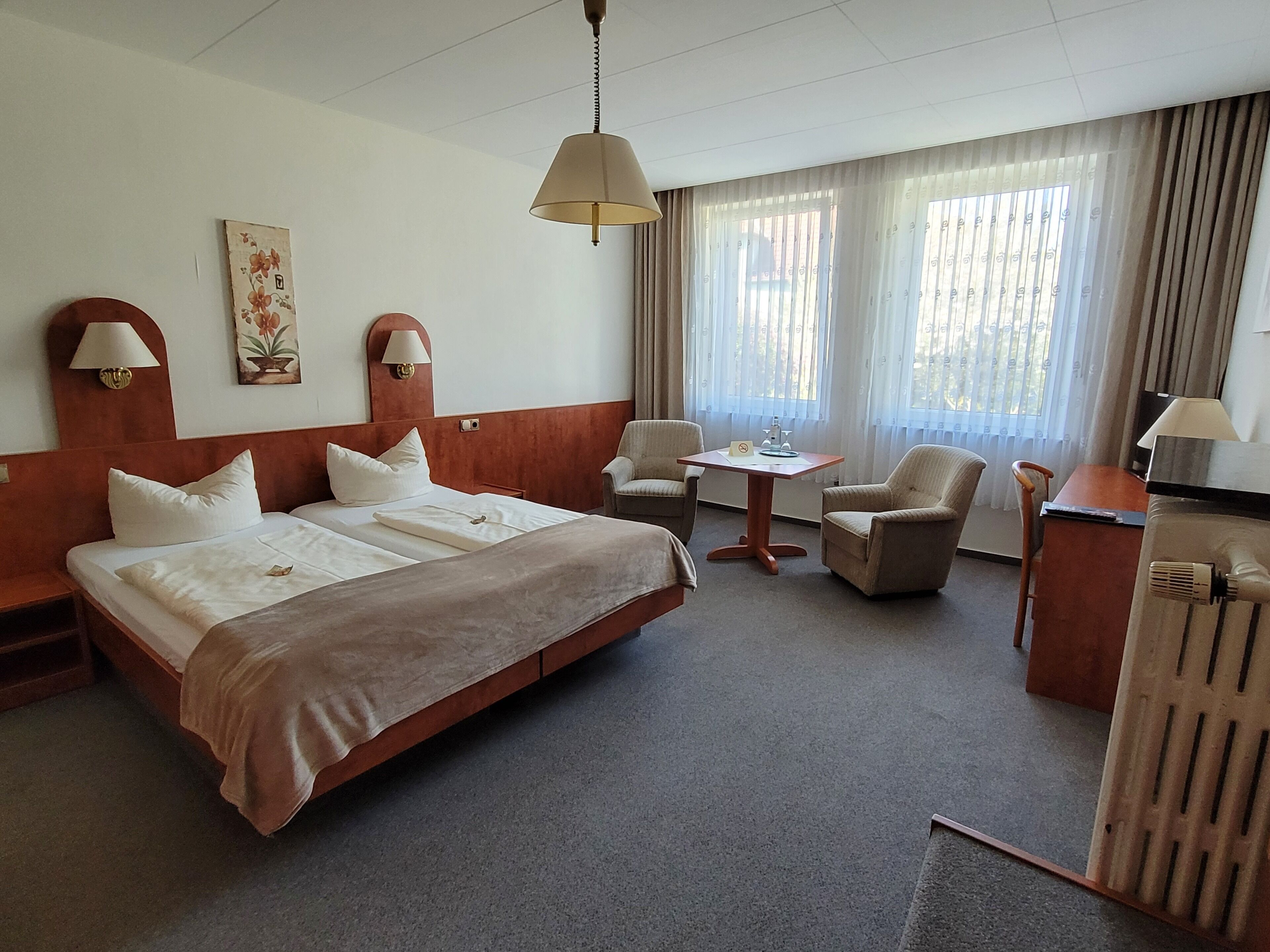 A hotel room with a large bed, two bedside tables, a desk, a chair, and a small table with a lamp.