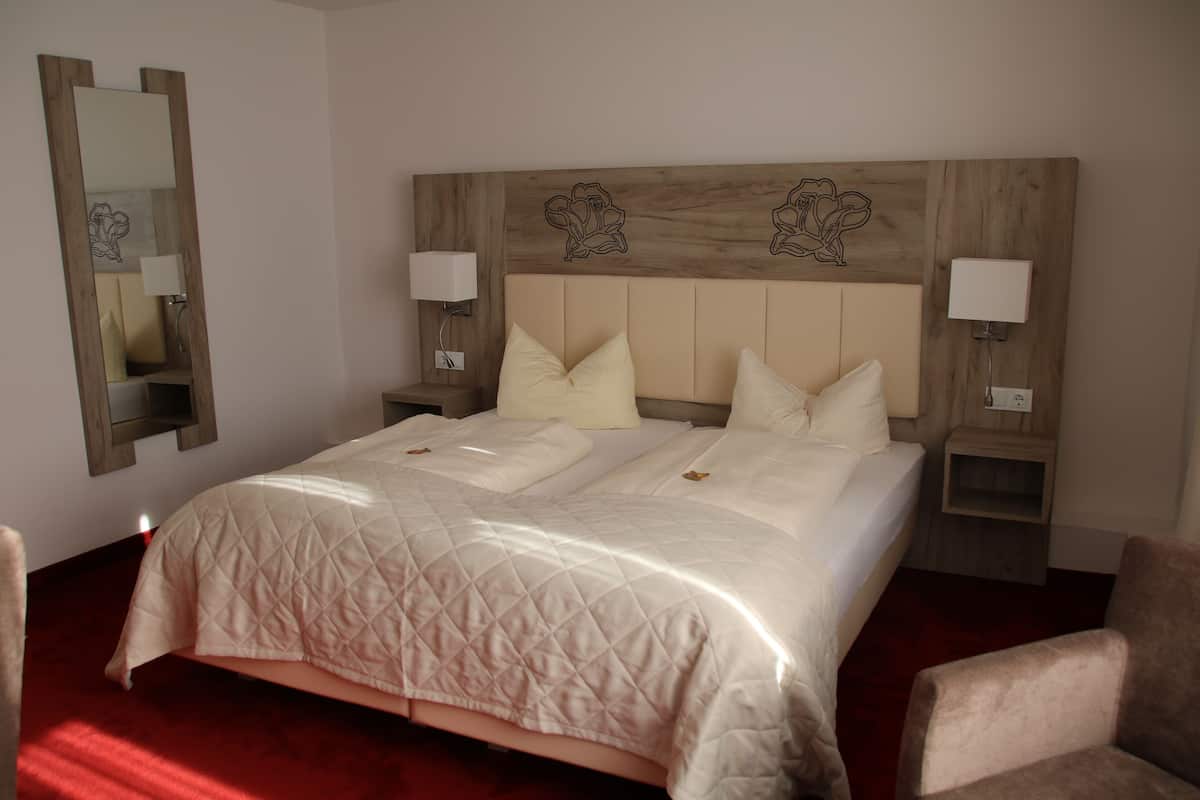 A hotel room with a large bed, two bedside tables with lamps, a wooden headboard with floral designs, and a red carpet.