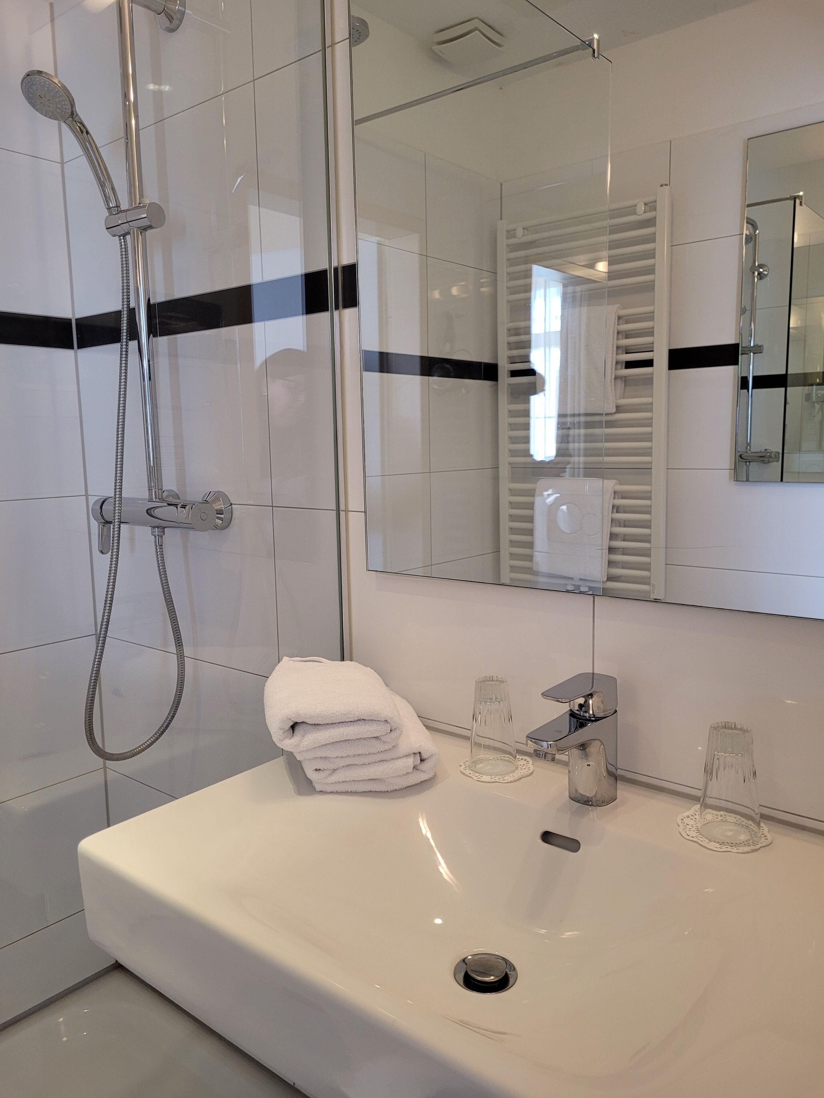 A modern bathroom with a glass-enclosed shower, a white sink, and a mirror with a black stripe.