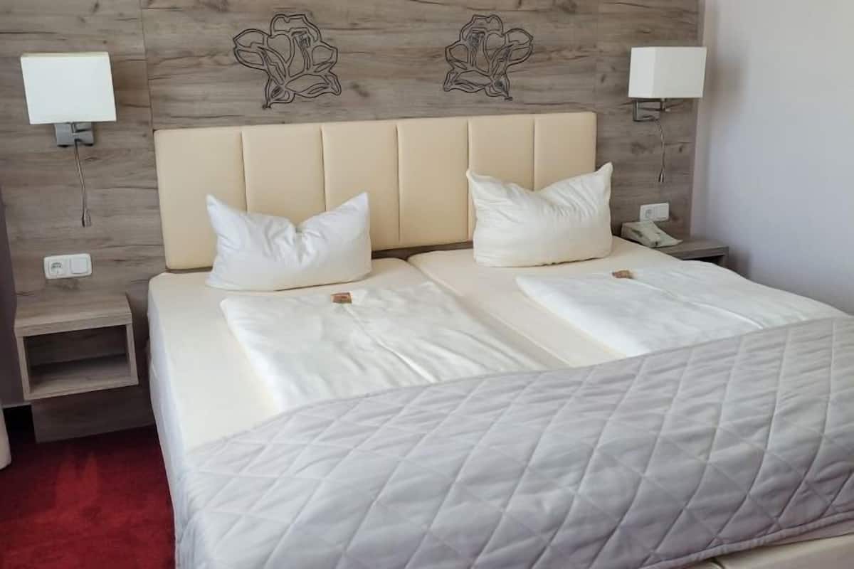 A double bed with white bedding, a wooden headboard, bedside lamps, and a nightstand with a phone.
