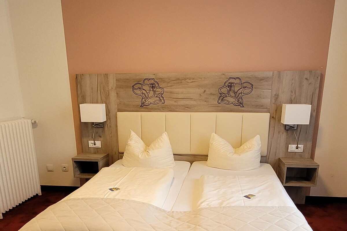 Una cama bien hecha con cubrecama acolchado, dos mesitas de noche con lámparas y un cabecero de madera con diseños florales.