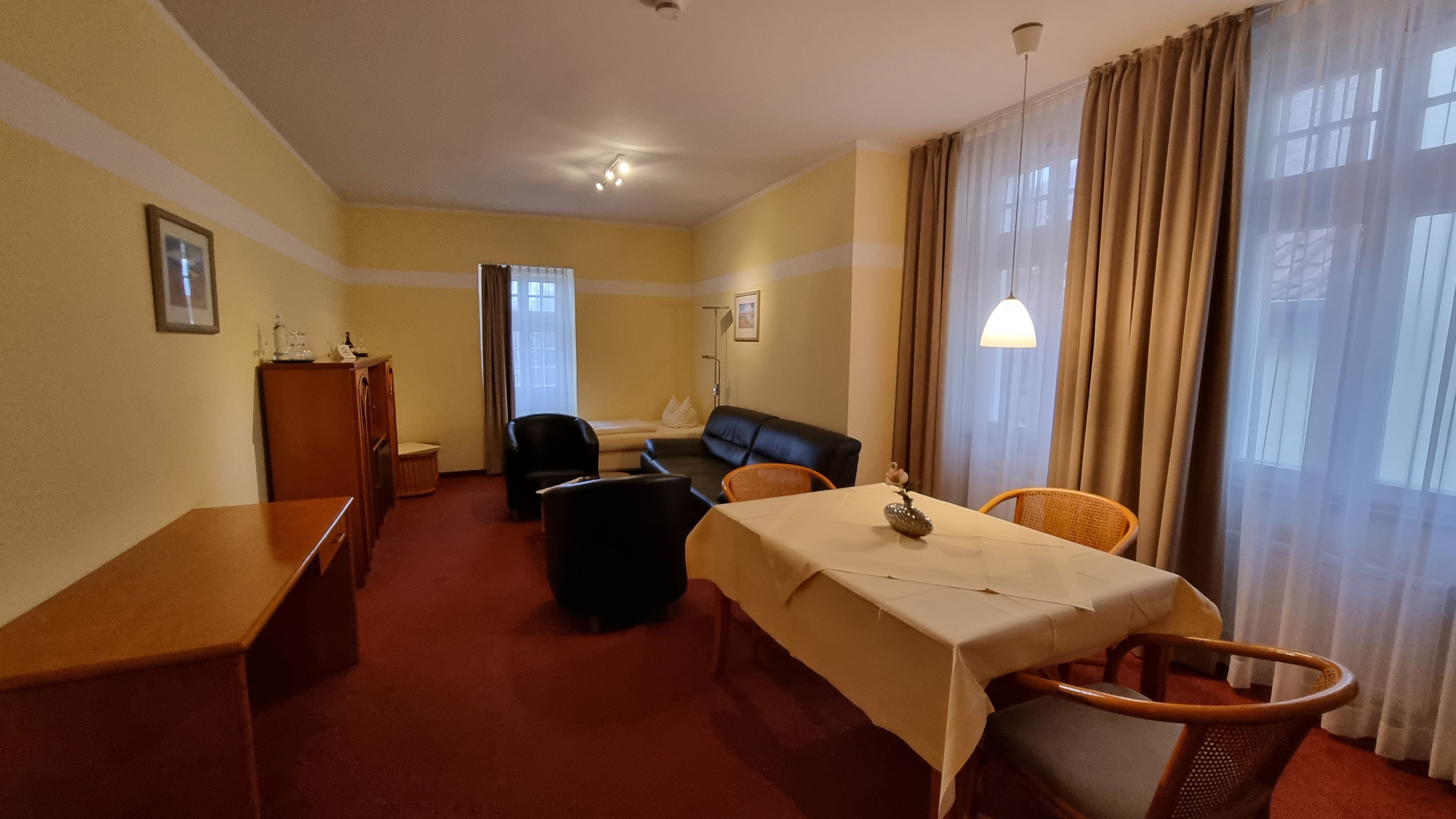 Ein Hotelzimmer mit Bett, Schreibtisch, Sessel, Sofa und Esstisch.