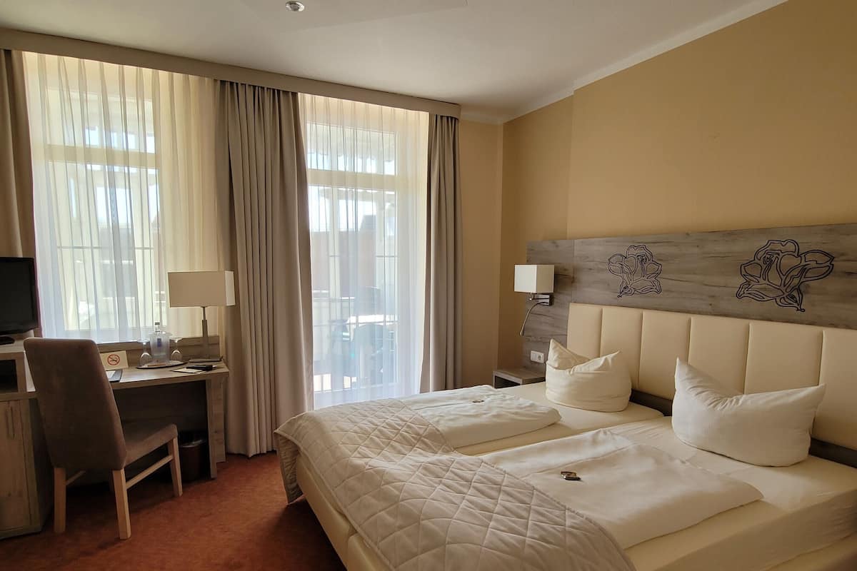 A hotel room with a large bed, a desk with a chair, a television, and a window with curtains.