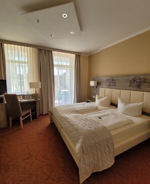 A hotel room with a large bed, a desk with a chair, a television, and a window with curtains. - Hotel Rosengarten (Bad Salzuflen)