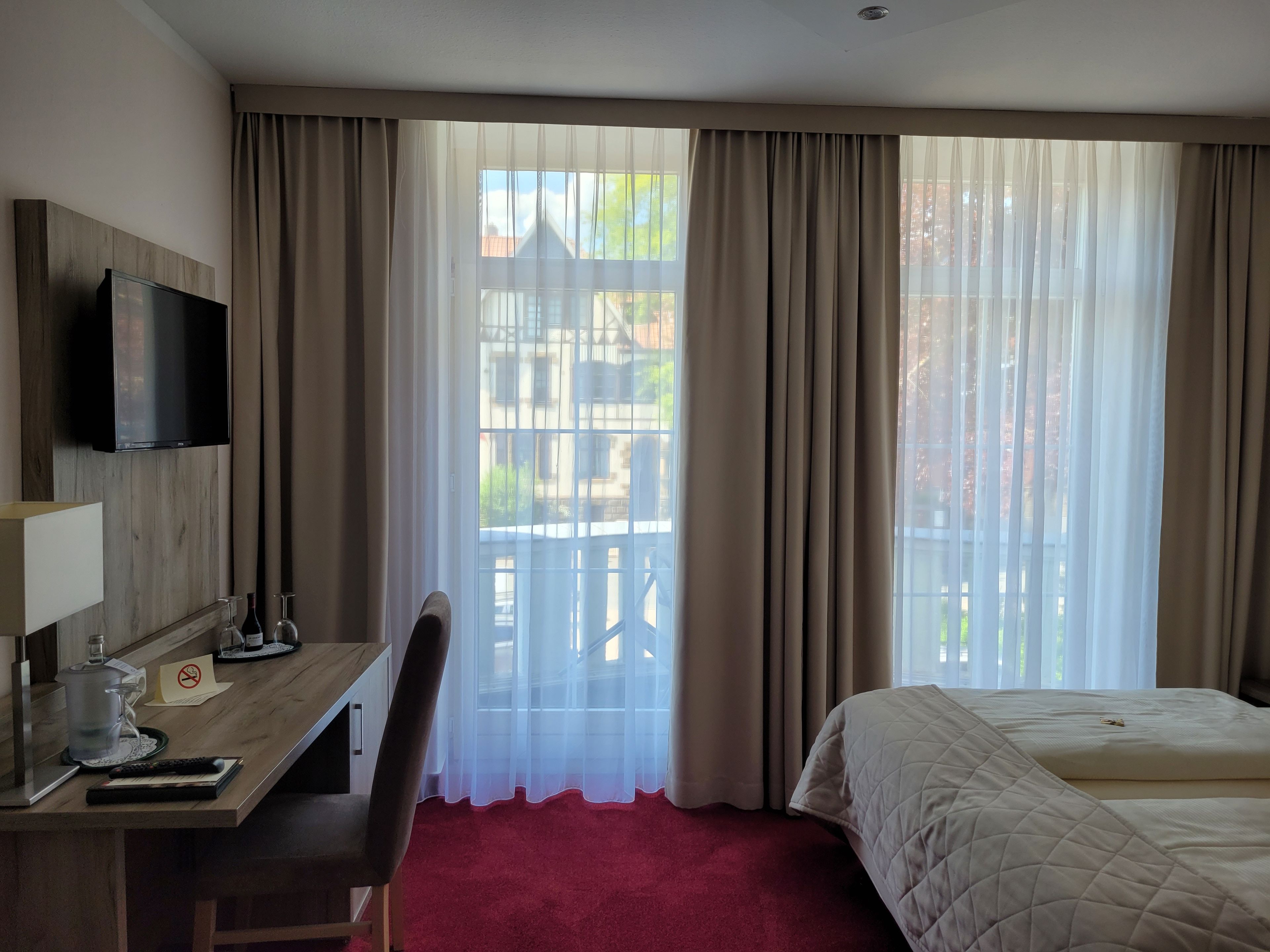 Habitación de hotel con cama, escritorio con televisor, una silla y ventana con cortinas.