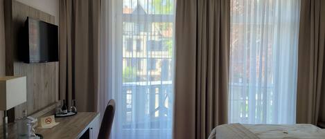Habitación de hotel con cama, escritorio con televisor, una silla y ventana con cortinas.