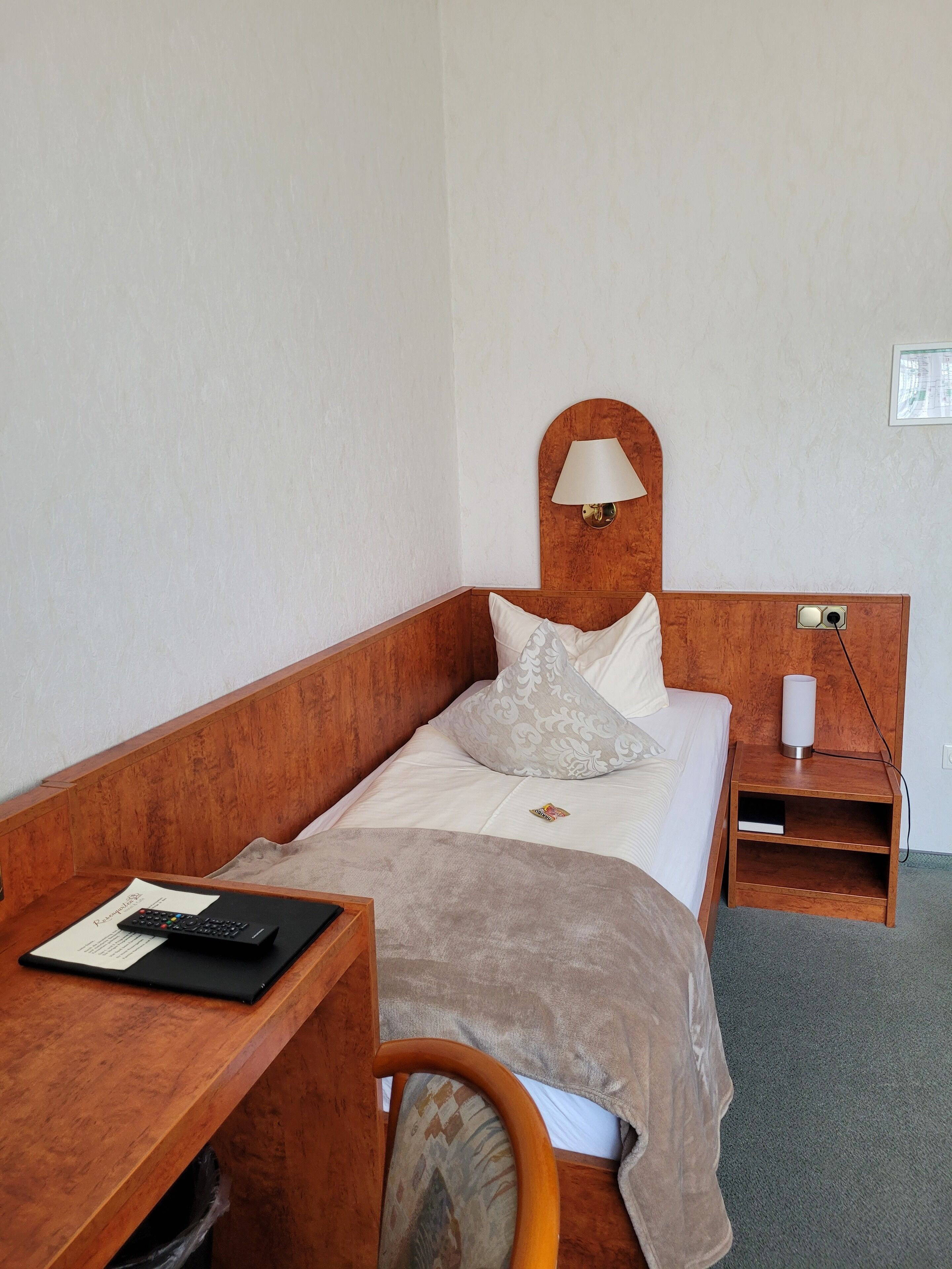 A single bed with a wooden headboard, a bedside table with a lamp, and a chair.