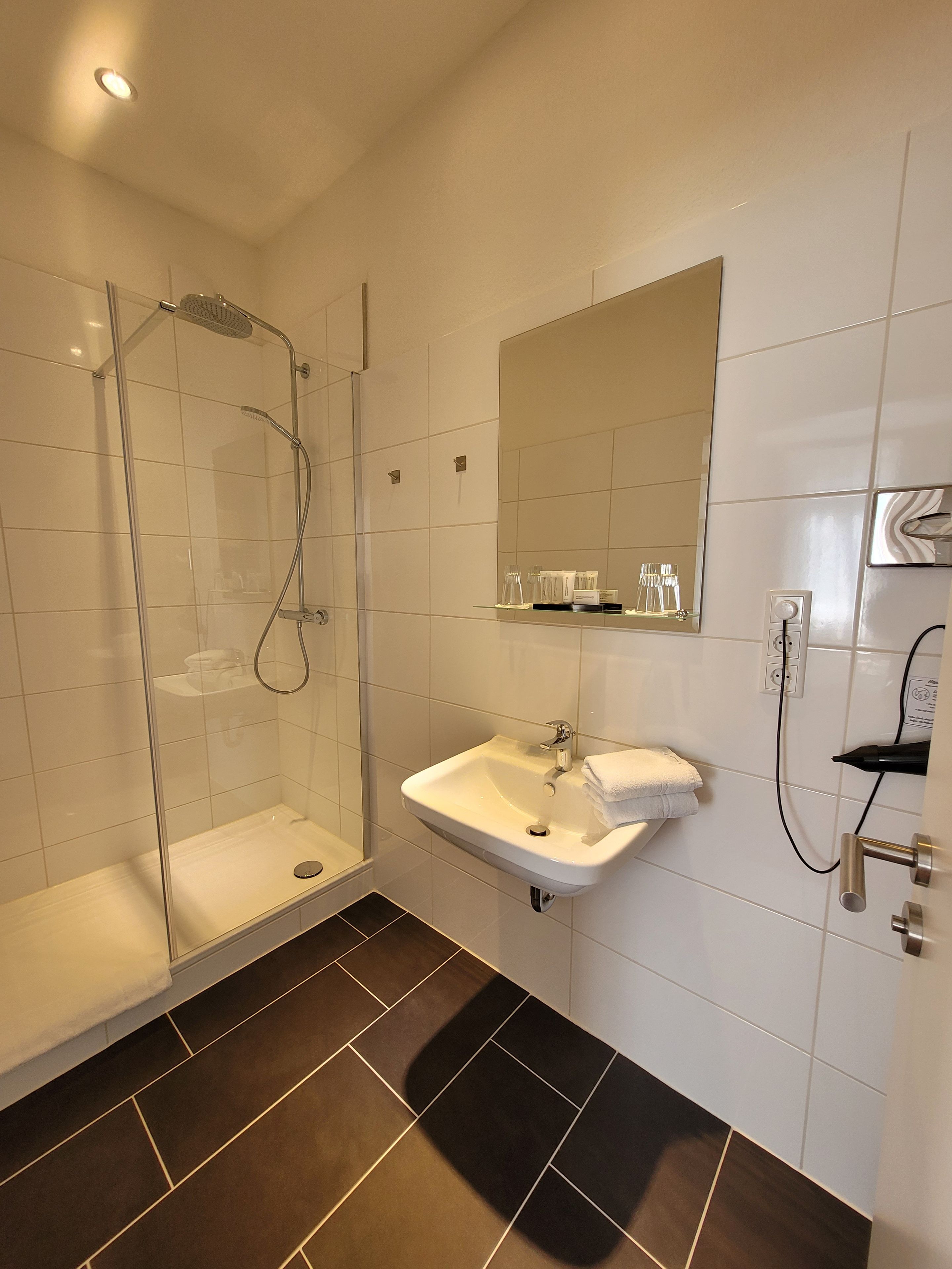 Une salle de bain moderne avec une douche à parois de verre, un lavabo blanc et un miroir au-dessus.