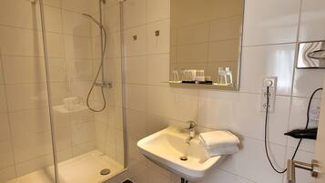 Un baño moderno con ducha envuelta en vidrio, un lavabo blanco y un espejo encima.