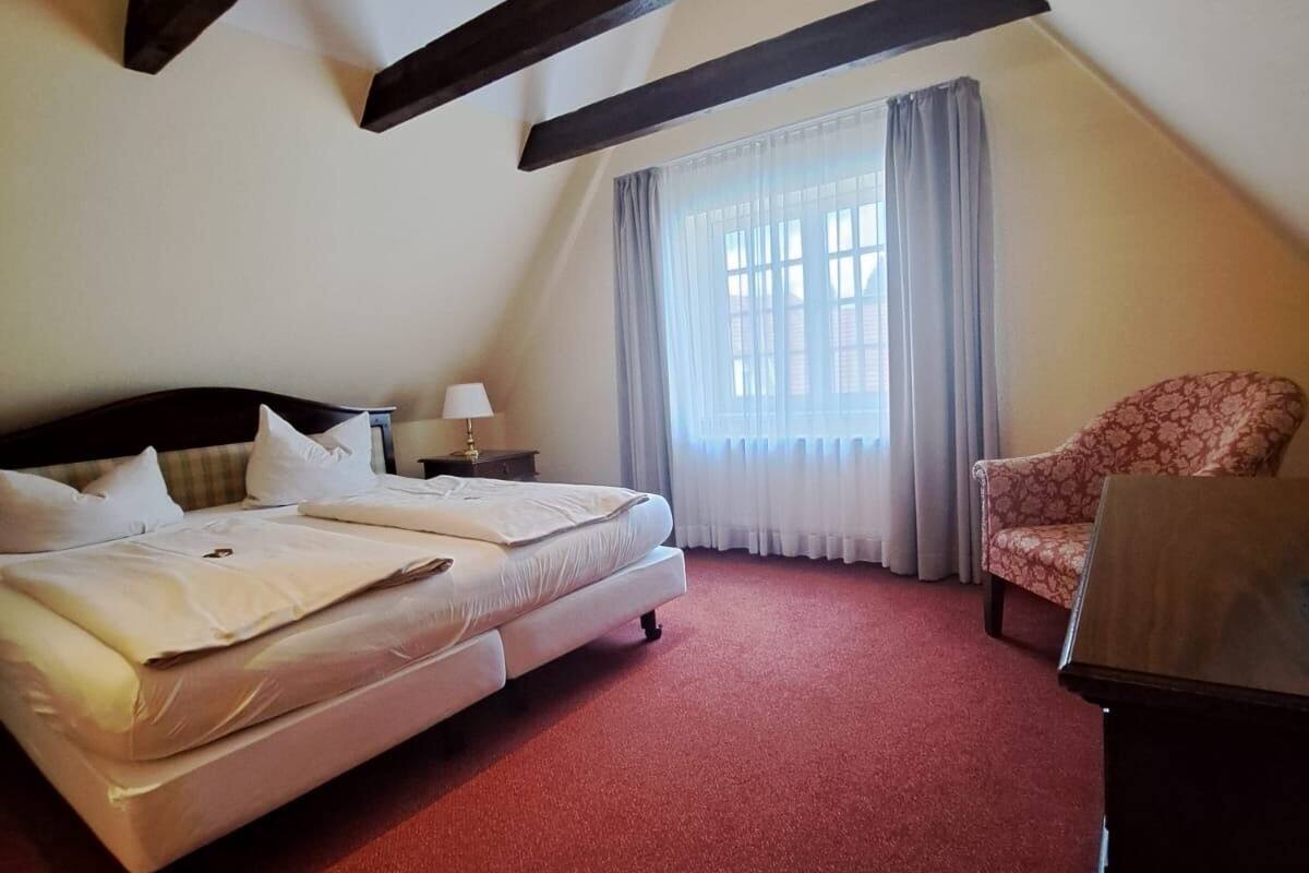 A room with a bed, a chair, a desk, and a window with curtains.