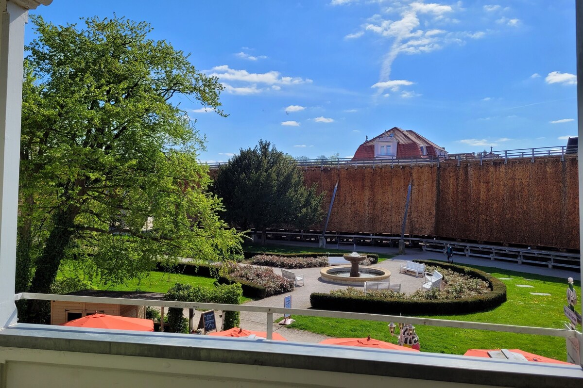 Vista de un patio con una fuente, zonas de estar y un edificio de techo rojo.