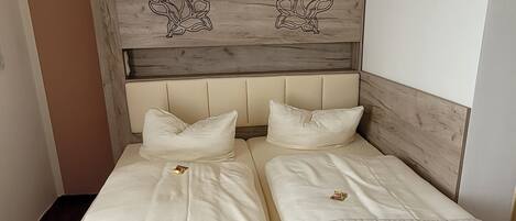 Un lit double avec une couette blanche matelassée et deux oreillers, une tête de lit en bois ornée de motifs floraux sculptés, et un mur sobre en arrière-plan.