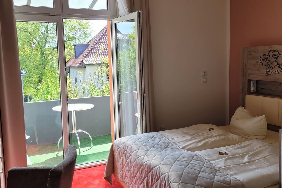 A hotel room with a bed, a chair, and a view of the outside.