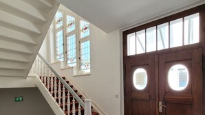 A staircase with white balusters, a red carpeted landing, and a wooden door with two windows. - Hotel Rosengarten (Bad Salzuflen)