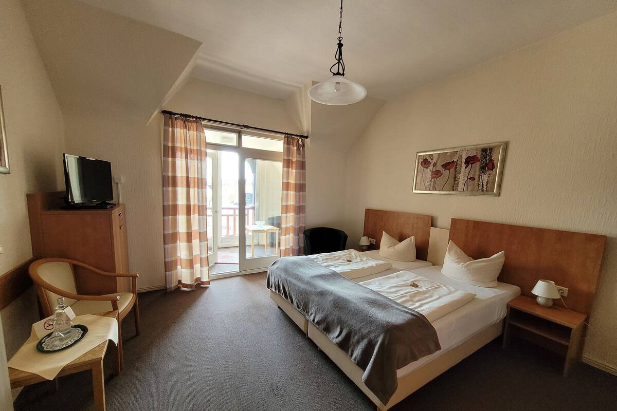 A hotel room with a bed, a desk, a chair, a television, a lamp, and a painting on the wall.