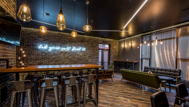 A modern bar area with a neon sign, wooden bar counter, metal chairs, and a green sofa. - Aster Hotel Group (Tashkent)