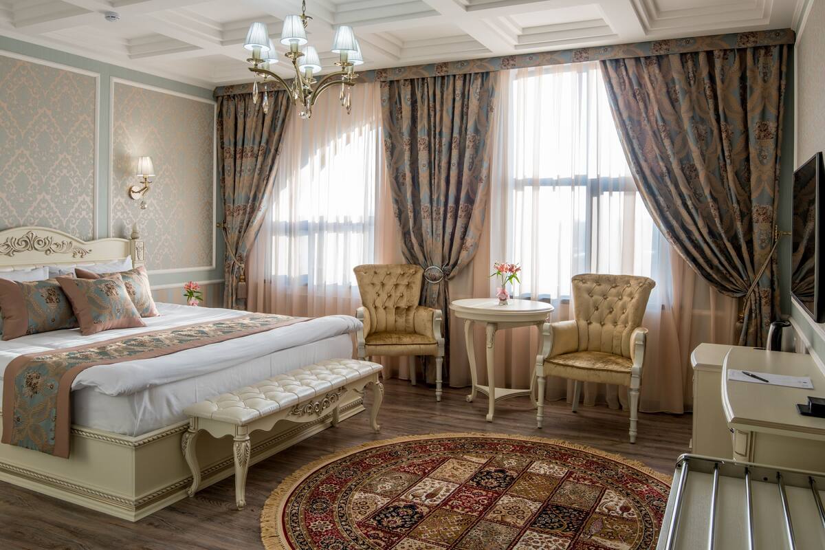 Ein geräumiges Schlafzimmer mit einem großen Bett, zwei Sesseln, einem kleinen runden Tisch und einem Schreibtisch.