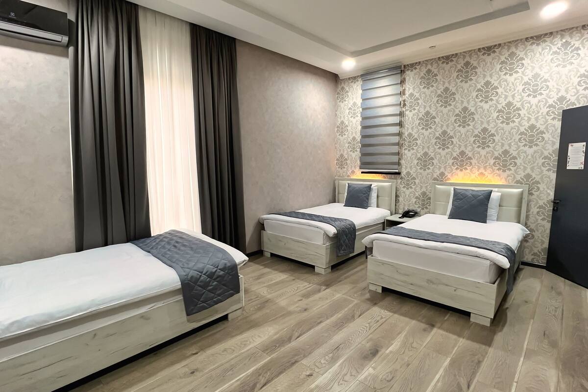 Ein Hotelzimmer mit zwei Einzelbetten, einem kleinen Nachttisch mit Lampe, einer Wandklimaanlage und einem Wandpapier mit Muster.