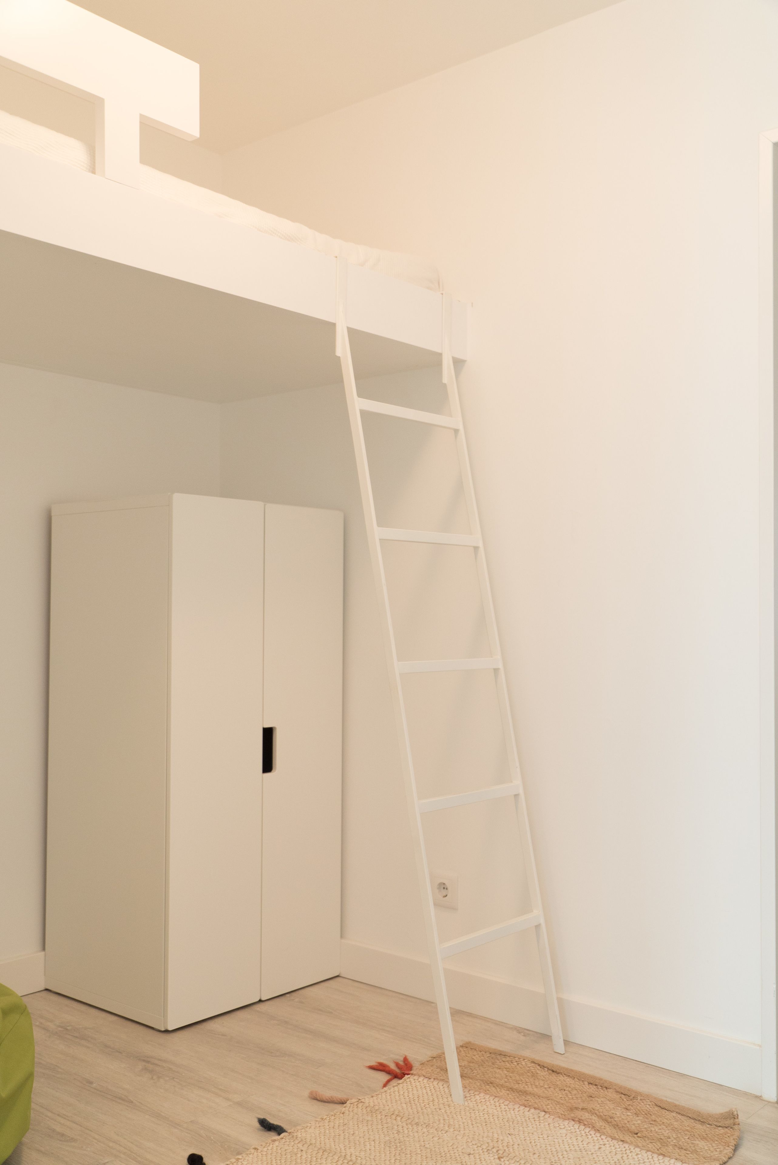 A room with a white wardrobe, a white ladder, and a wooden floor.