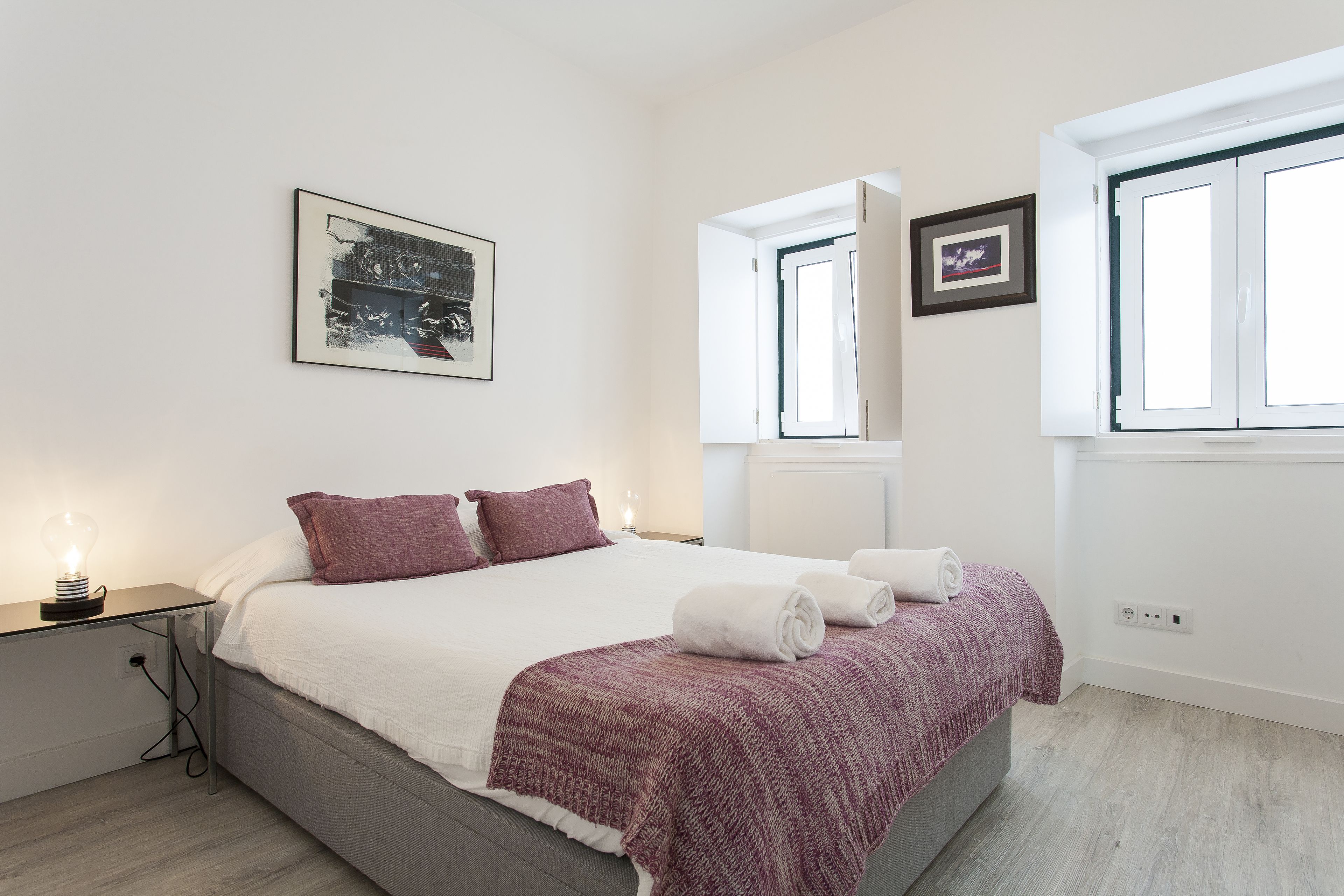 A bedroom with a bed, a nightstand, a lamp, and a window.