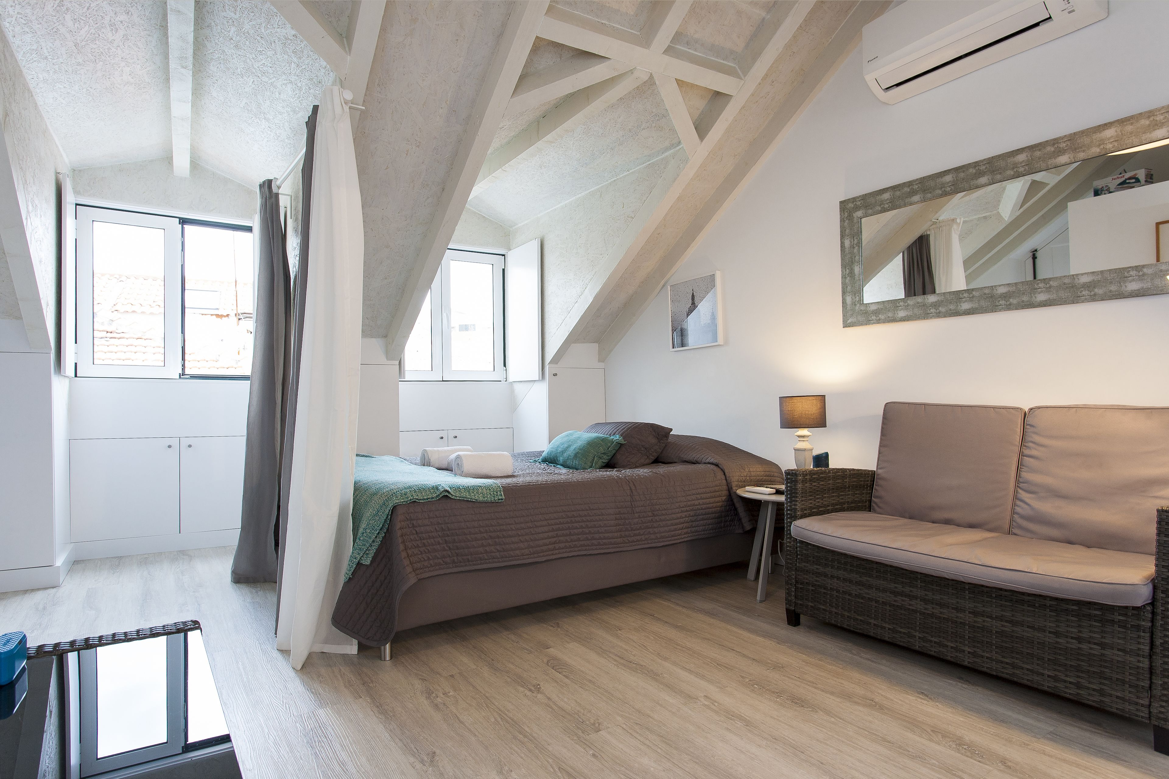 A bedroom with a bed, a sofa, a small table, and a mirror.