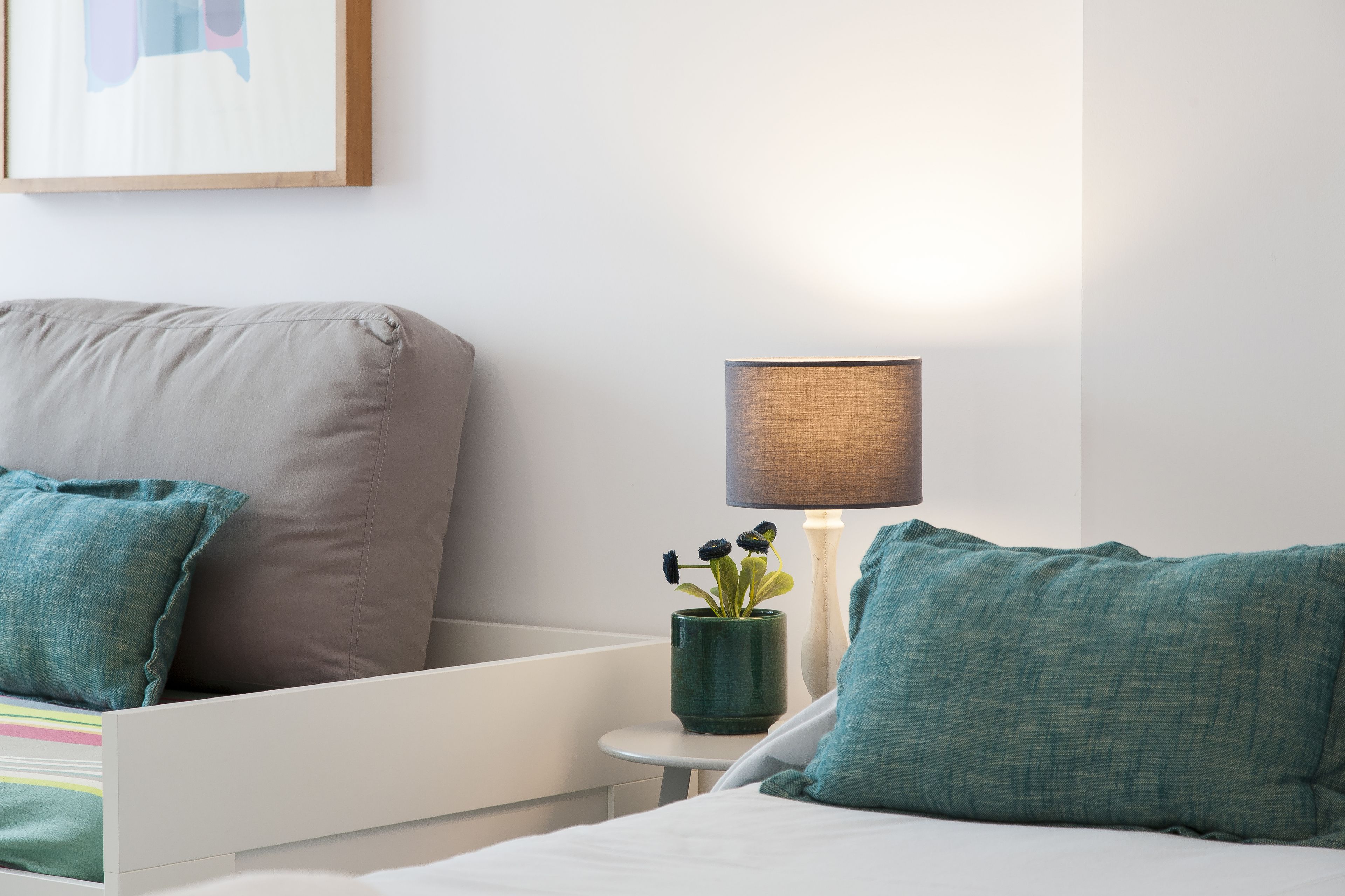 A modern bedroom with a bed, a bedside table with a lamp, and a wall-mounted artwork.