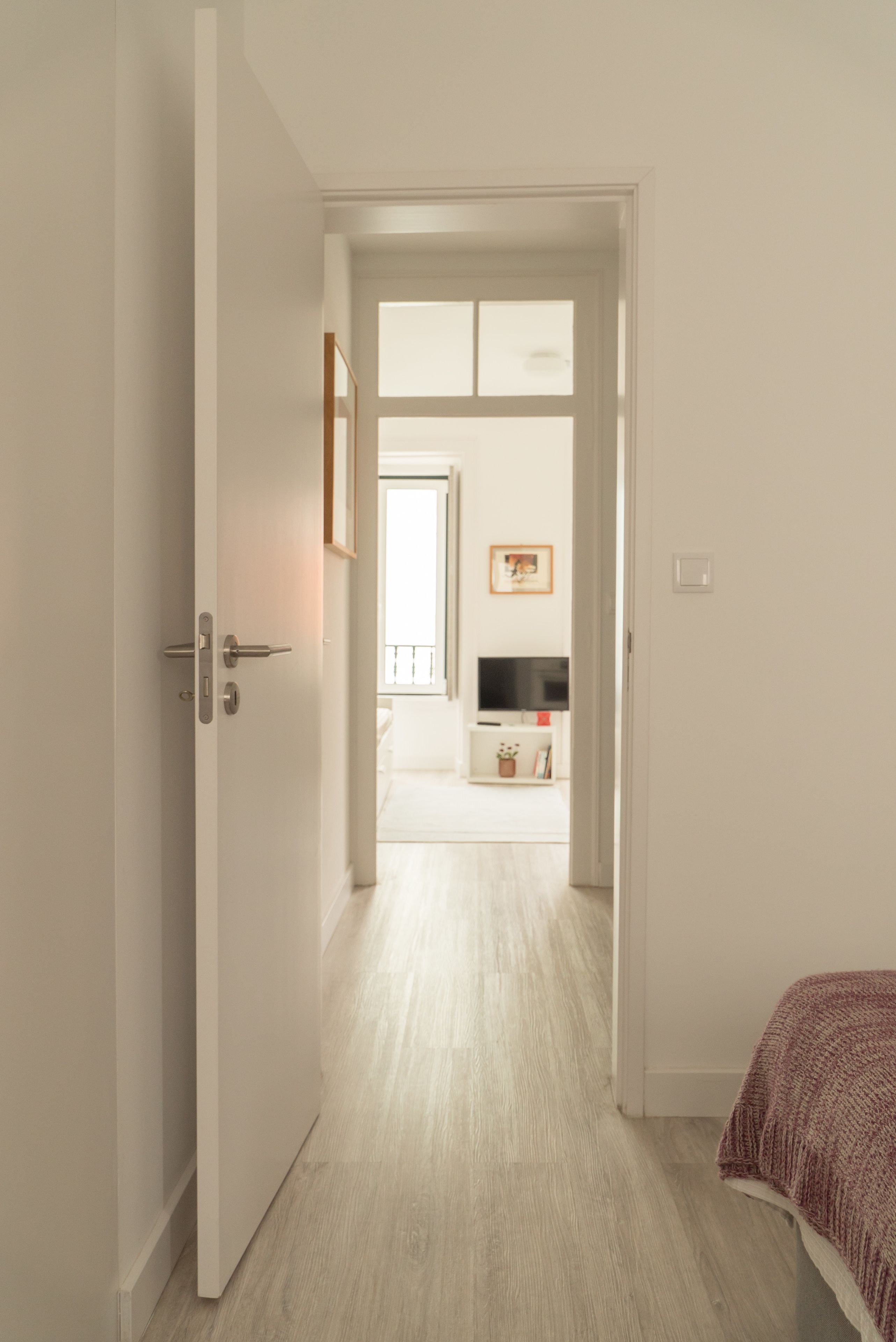 A hallway leading to a bedroom with a bed, a TV, and a small table with a plant.