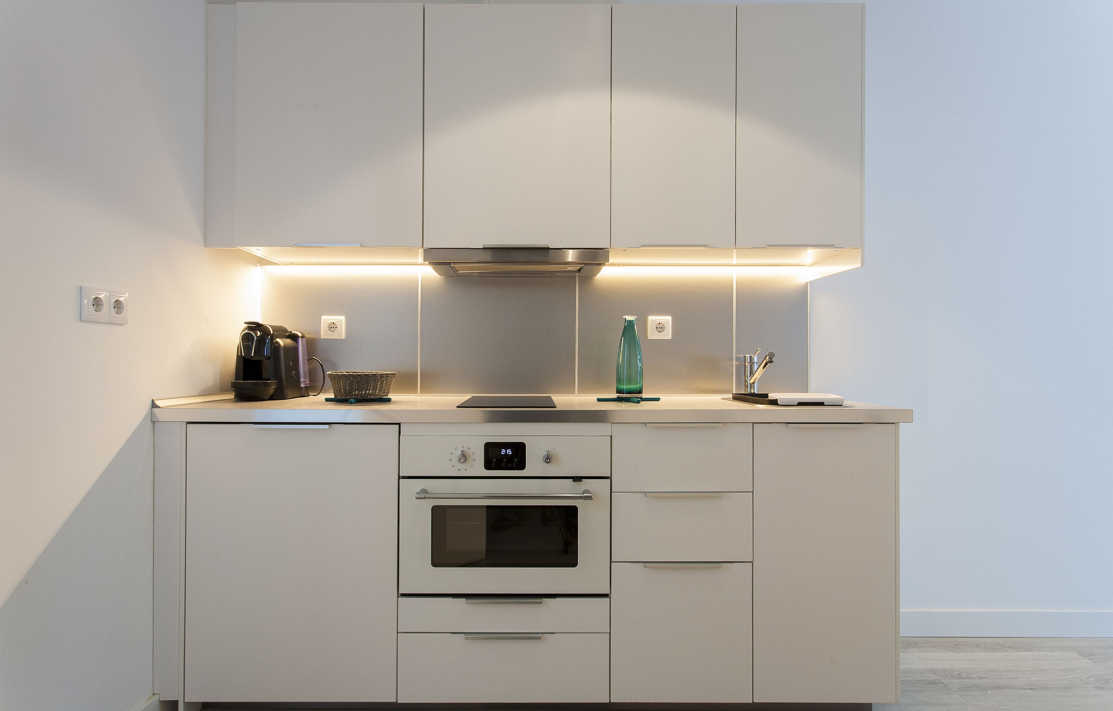 Une cuisine moderne dotée d’appareils électroménagers intégrés, d’une hotte en acier inoxydable et d’un éclairage sous les meubles hauts.
