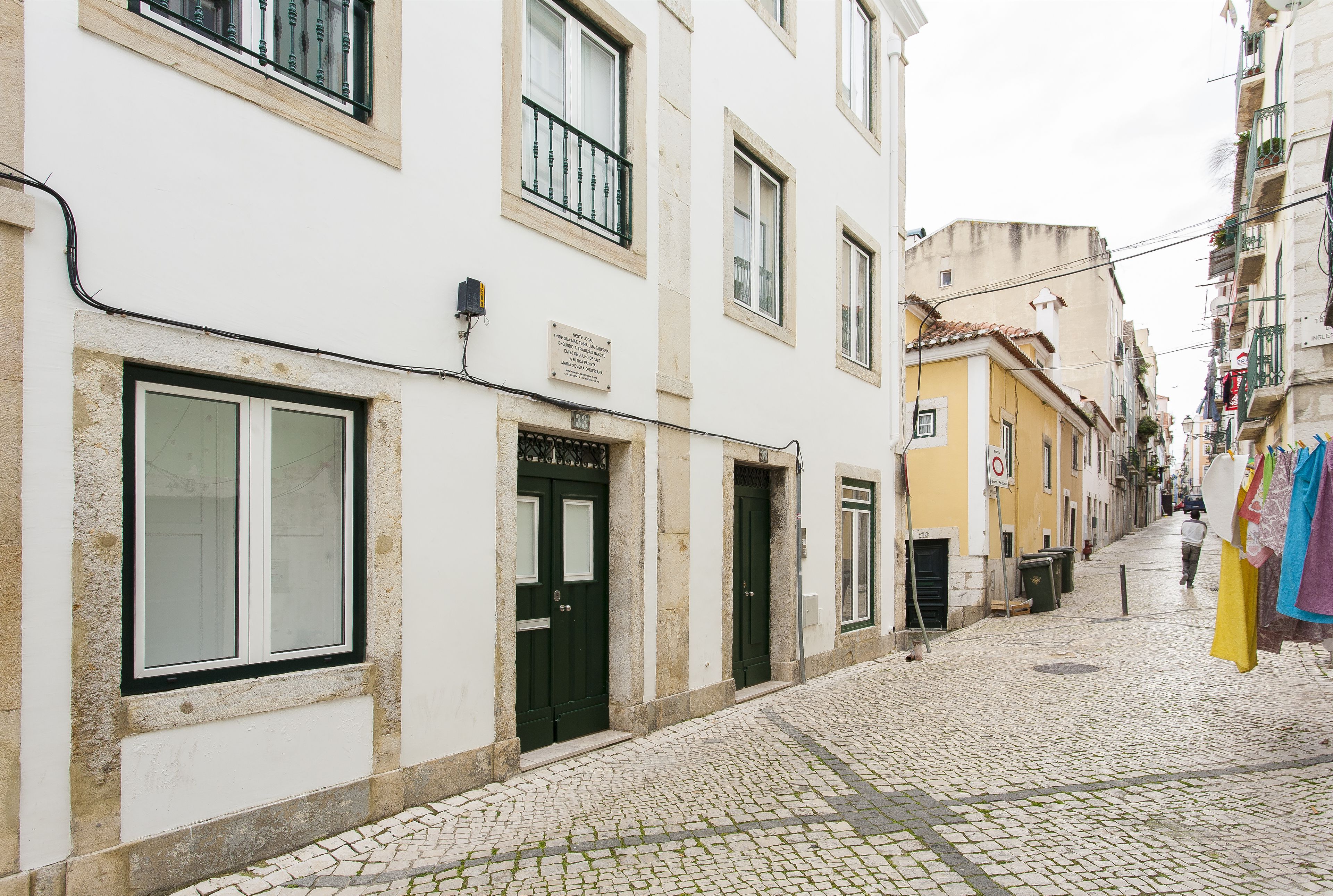 Une ruelle étroite pavée, bordée d’immeubles, dont certains sont dotés de balcons et de portes.