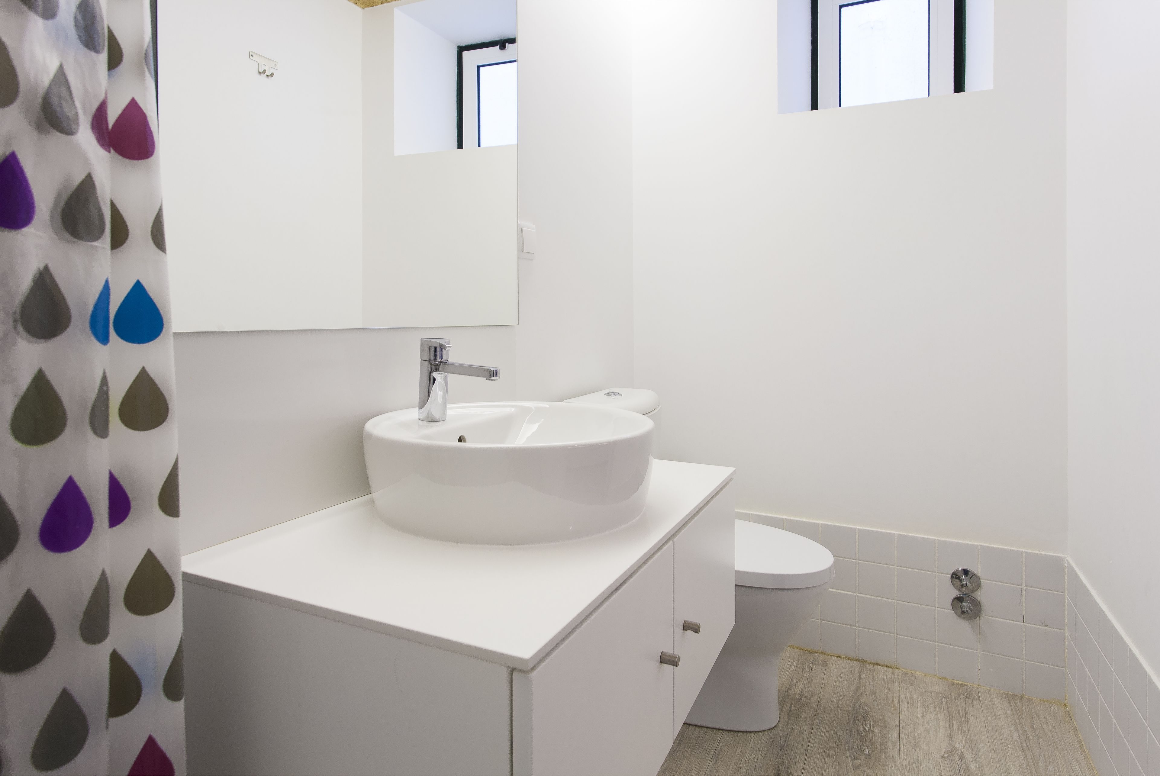 Un bany modern amb un lavabo blanc, un mirall i un vàter.