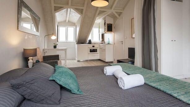 A bedroom with a large bed, a desk, and a kitchenette. - Severa Apartments (Lisbon)